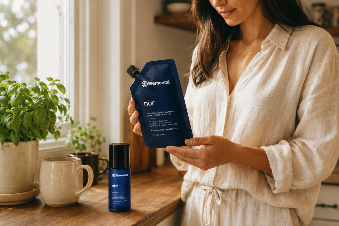 Woman holding an Elemental nūr biodegradable refill pouch in a kitchen, with the nūr deodorant bottle on the counter