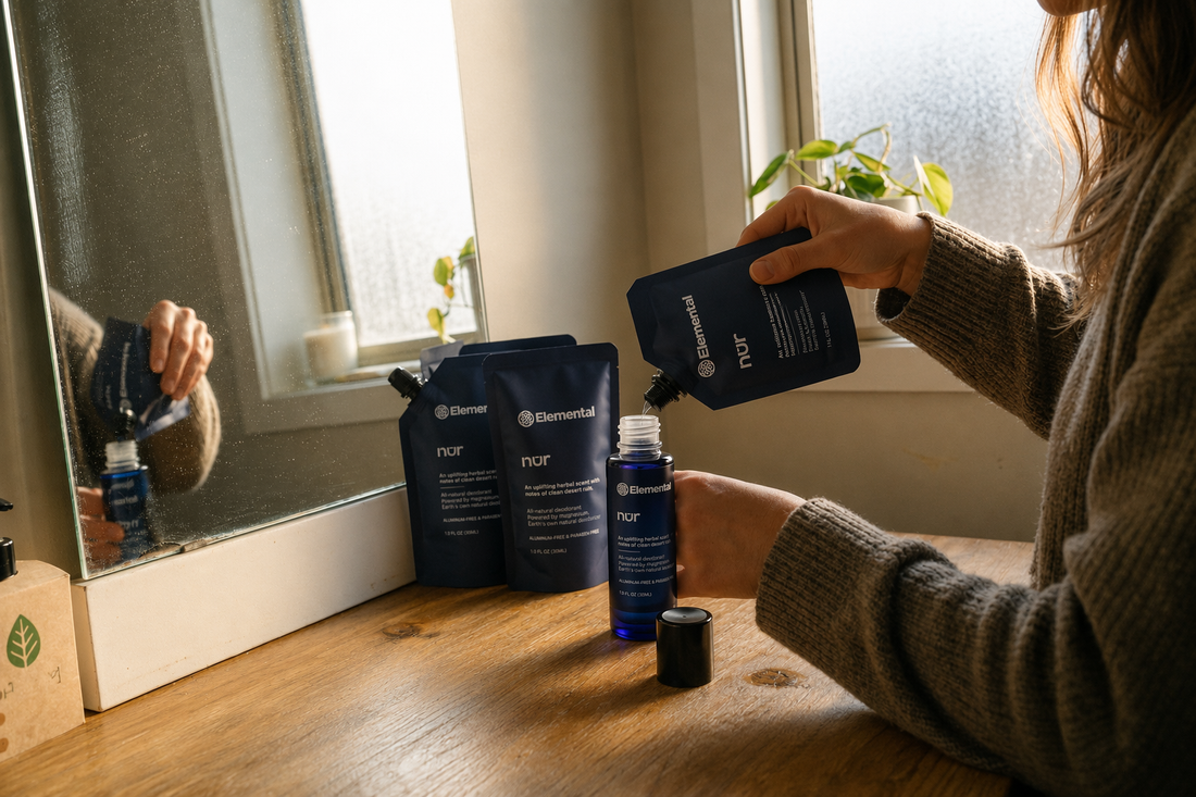 Refilling an Elemental nur deodorant bottle from a refillable navy pouch at a sunlit vanity